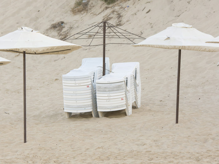 Two stacks of folded chairs on the beach with umbrellas