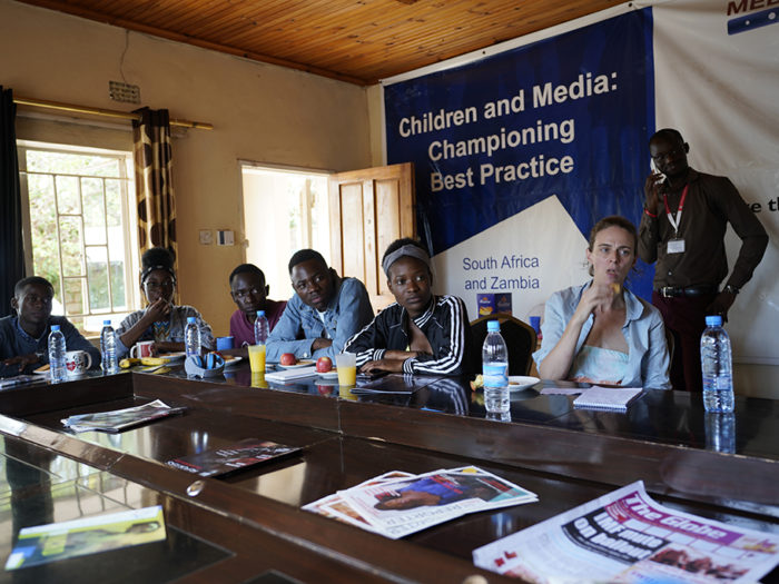 Redaktionen sitter vid stort mötesbord. Banderoll i bakgrunden "Children and Media: Championing Best Practice"..